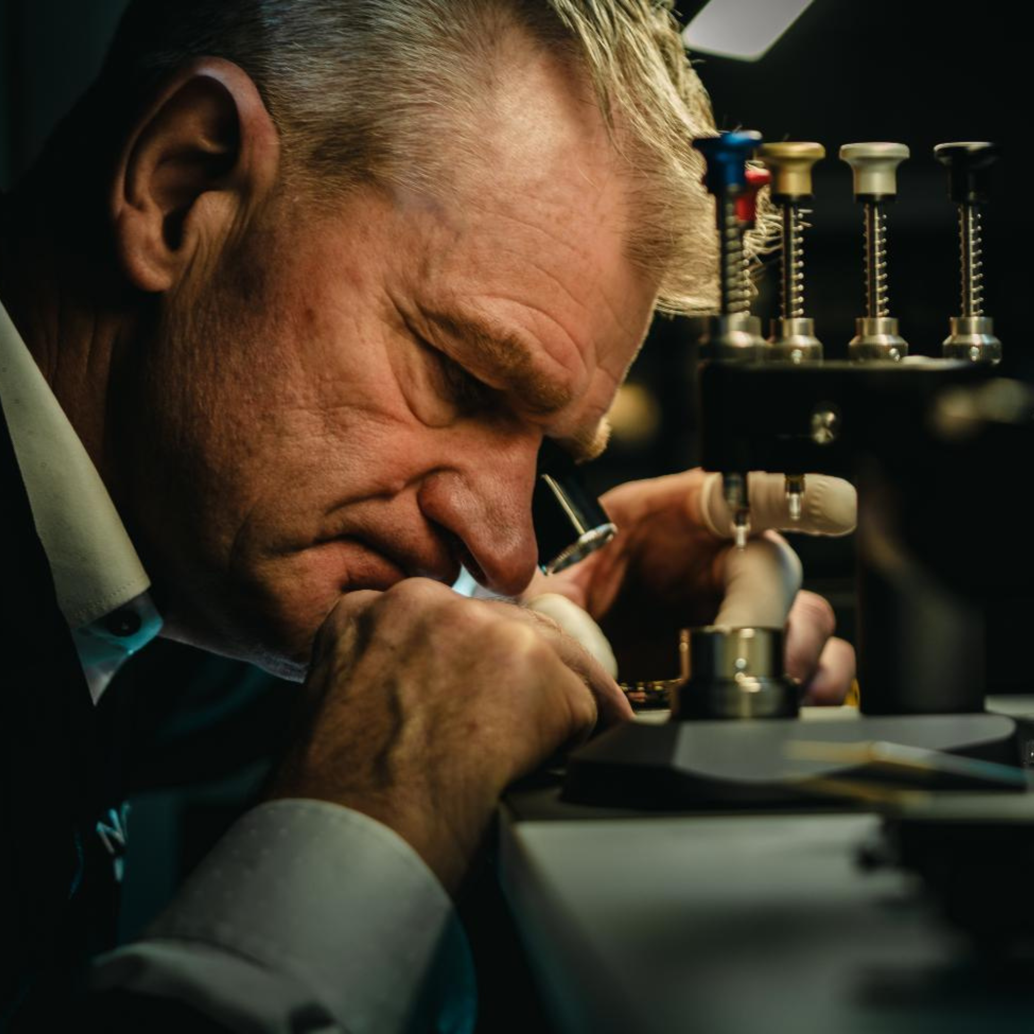Man examining watch parts under a magnifying glass in a workshop.